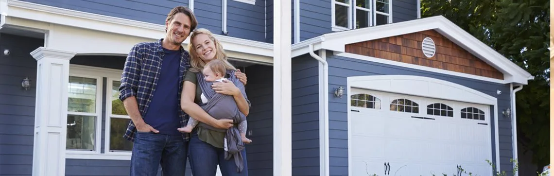 Smiling couple with a baby standing in front of their house.