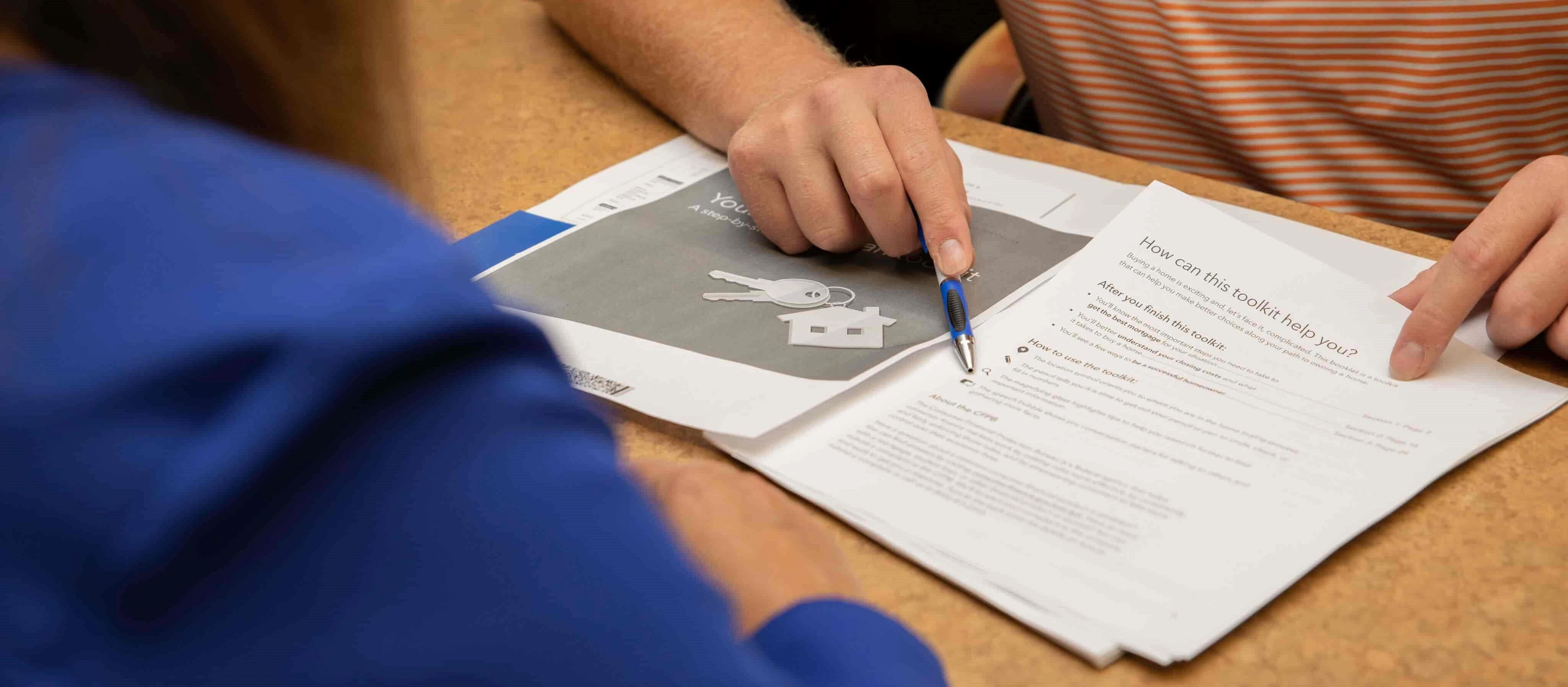 Person pointing at home loan documents during a discussion.